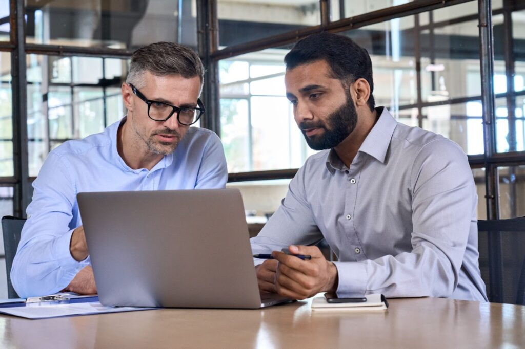 Two operations research analysts discussing while looking at a laptop screen