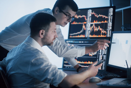 Two operations research analysts discussing data displayed across multiple monitors