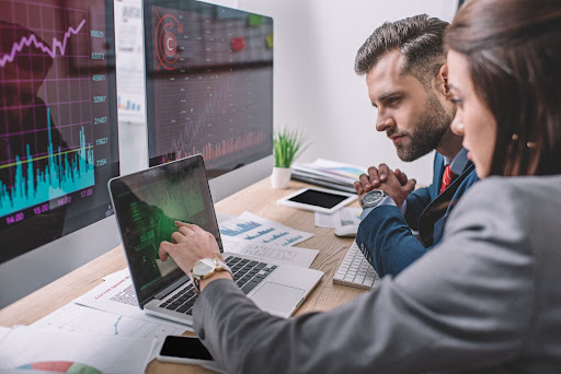 Two operations research analysts talking about data results while one gestures to a graph on a laptop